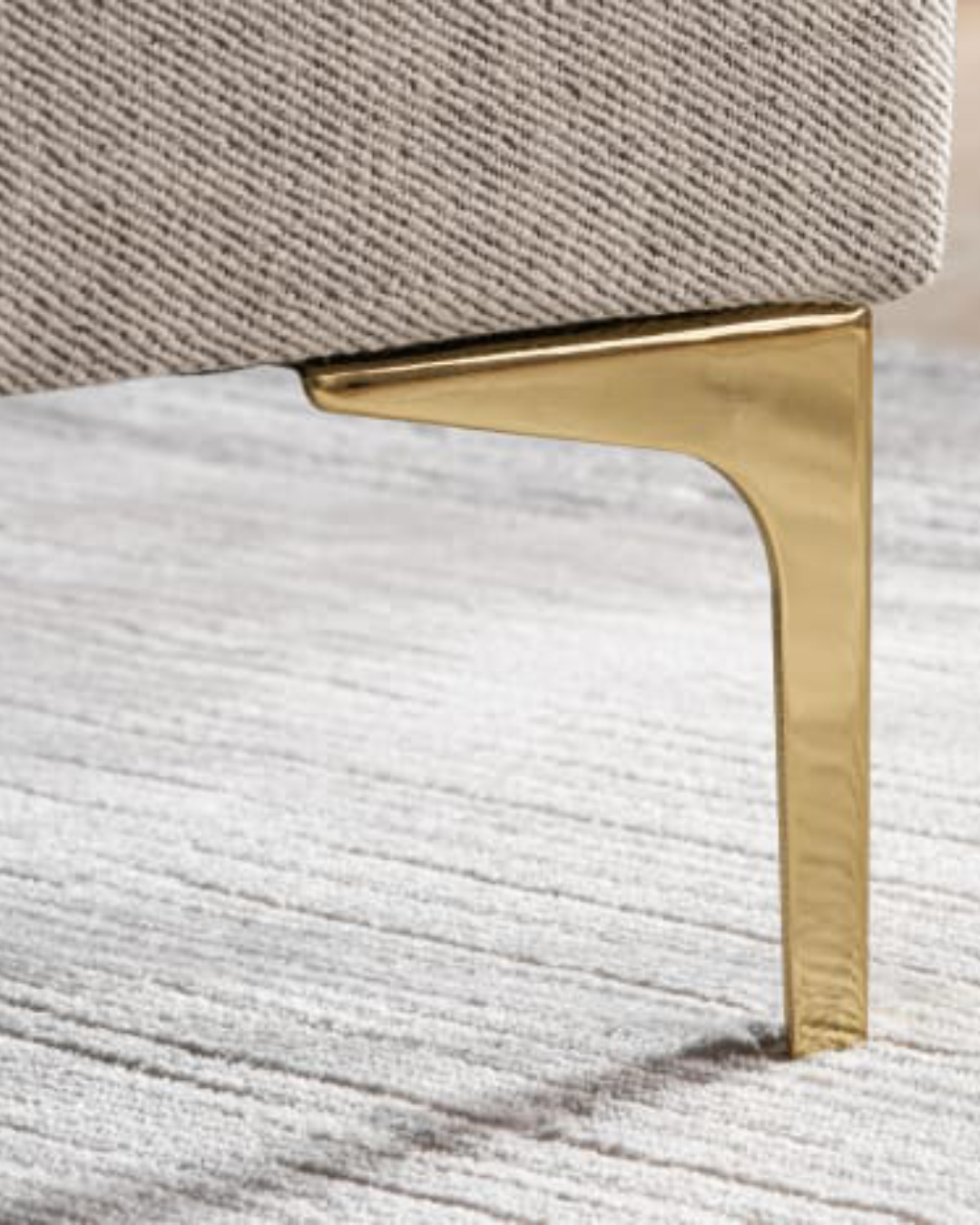 Close-up of curved slim leg detail under Carrcroft footstool showing gold tone finish
