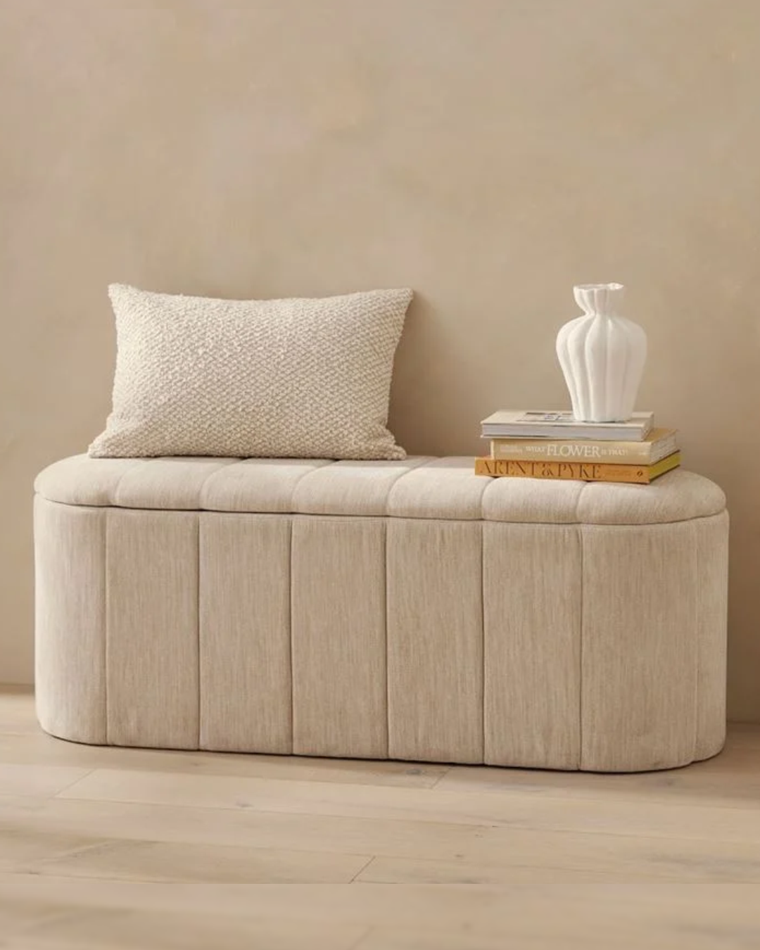 Front angle of Isenbrook ottoman box showing vertical fluted panels and smooth beige fabric upholstery.