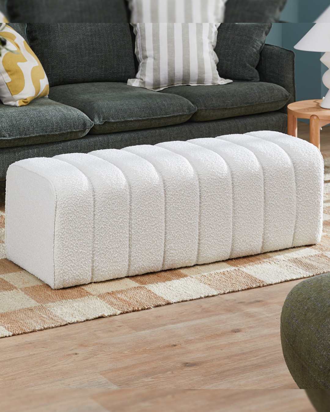 Side angle of curved boucle accent footstool with soft segmented upholstery and low silhouette.