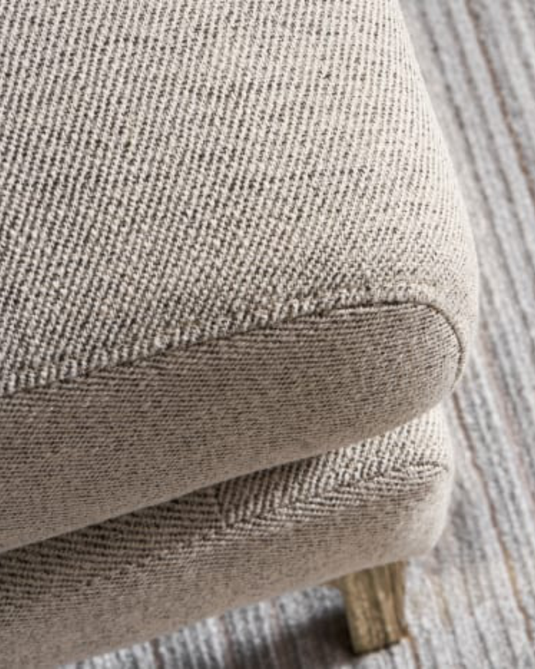 Top corner view showing textured taupe fabric and soft edge profile of Carrcroft footstool